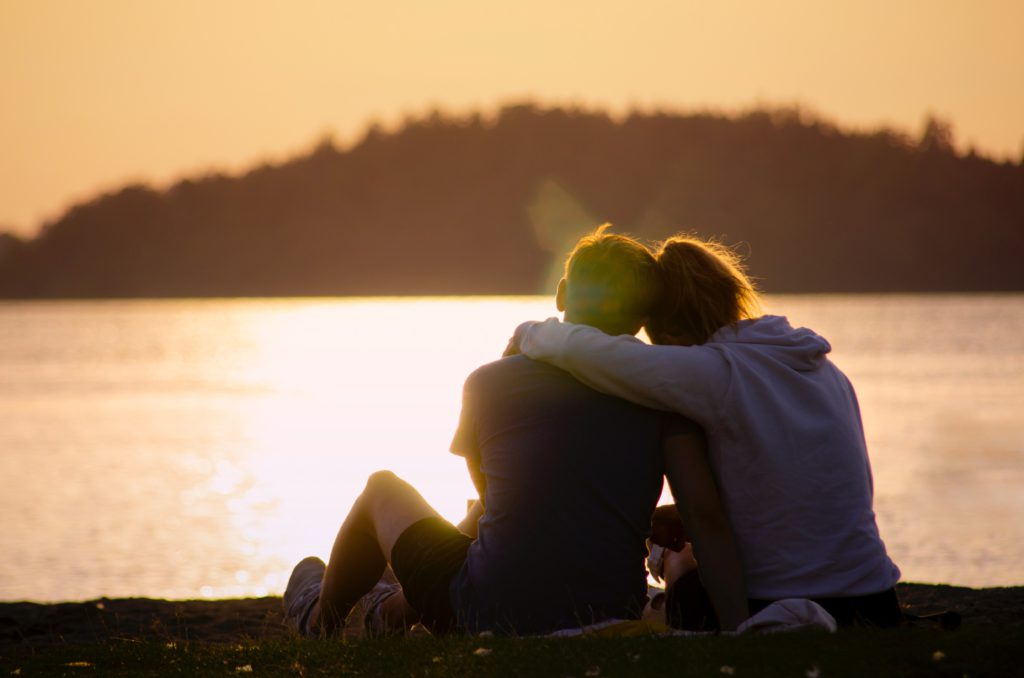 Two people sitting together and hugging while facing a water body