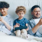 Parents sitting next to a child, playing on their phones